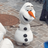 a snowman with a carrot nose is standing on a cobblestone sidewalk