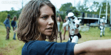 a woman in a blue shirt is standing in a field with a group of people in the background .