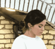 a woman in a white shirt is standing in front of a brick wall .