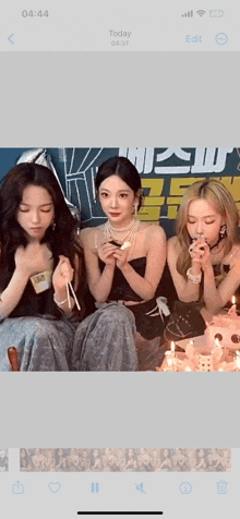 three women are sitting in front of a cake with candles on it