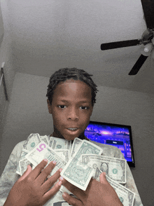 a young boy is holding a stack of dollar bills including a 5 dollar bill