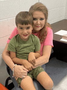 a woman in a pink shirt holds a young boy in her lap