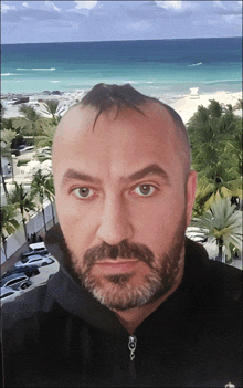 a man with a beard is looking at the camera with a beach in the background