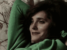 a woman in a green sweater is laying on a couch with her head on her arms .