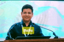 a man stands at a podium with the name babu written on it