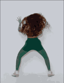 a woman is dancing in front of a white wall wearing green leggings and a green top .