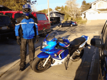 a man wearing a helmet stands next to a blue motorcycle with a license plate that says ' lgc '