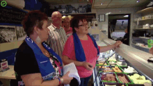 a woman wearing a scarf that says ' ucs ' on it stands in front of a display case of food