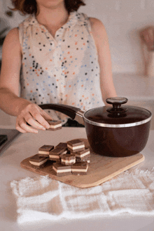 a woman in a polka dot shirt is cutting chocolate on a wooden cutting board