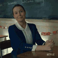 a woman sits at a desk with her hands folded in front of a blackboard that says south carolina on it