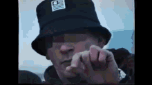 a man wearing a black bucket hat is making a peace sign .