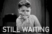 a black and white photo of a little boy sitting at a desk with the words `` still waiting '' .