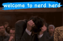 a man with his head in his hands is sitting in front of a sign that says welcome to nerd here