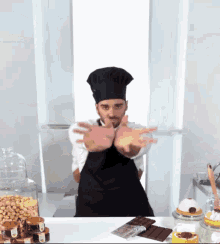 a man in a chef 's hat and apron is standing in front of a table full of nuts and desserts