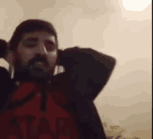 a man with a beard is standing in a room wearing headphones and a red shirt .