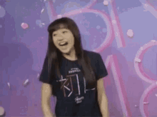 a woman in a black shirt is standing in front of a purple background with petals falling from the sky .