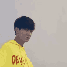 a young man wearing a yellow hoodie with the word devil on it is looking at the camera .