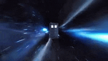 a police box is flying through a space tunnel with a blue light coming out of it .