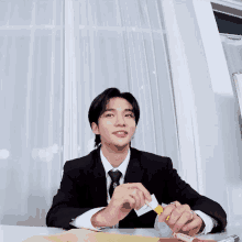 a young man in a suit and tie is sitting at a desk