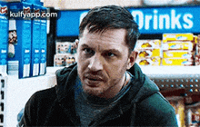 a man in a hoodie is standing in front of a drinks sign .