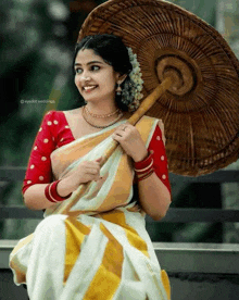 a woman in a white and yellow saree is holding a wicker umbrella .