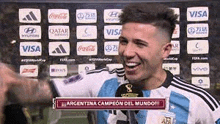 a soccer player is smiling and talking into a microphone while standing in front of a wall with advertisements .