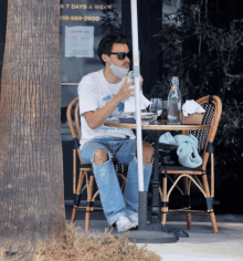 a man wearing a mask sits at a table with a sign that says 7 days a week on it