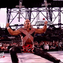 a wrestler is standing in front of a crowd with his arms in the air while wearing a red and white outfit .