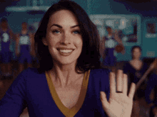 a cheerleader wearing a purple sweater and a yellow collar waves her hand