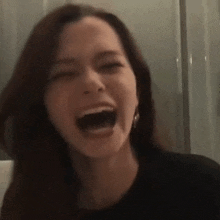 a woman in a black shirt is laughing with her mouth wide open