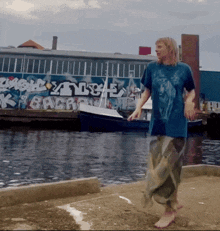 a woman in a blue shirt walks barefoot in front of a building with graffiti on it that says " back "