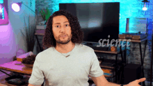 a man with curly hair and a beard is standing in front of a television with the word science on it