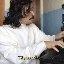 a man in a white shirt is typing on a laptop with the words ta passada written on the bottom