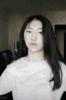 a girl with long black hair is wearing a white shirt and looking at the camera .