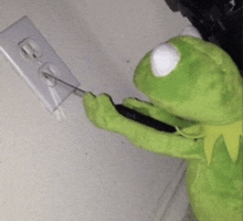 a stuffed kermit the frog is plugging something into an electrical outlet