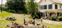 a group of people are standing in front of a house with a pile of wood in front of them .