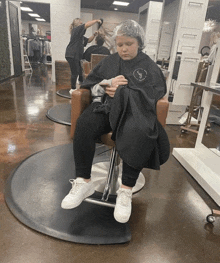 a woman in a black cape is sitting in a chair in a salon