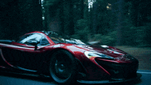 a red sports car is driving down a road with trees in the background