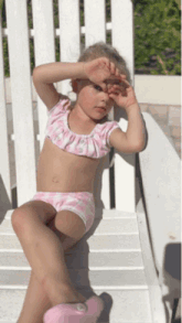 a little girl in a pink bikini sits on a chair