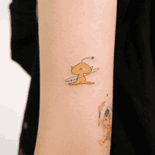 a small tattoo on a person 's arm of a yellow alien with a star on its head