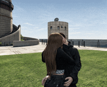 a man and a woman are kissing in front of a building with a clock on top of it