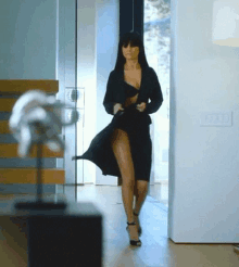 a woman in a black dress and high heels is walking through a doorway .