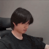 a young man in a black shirt is sitting in a chair and making a funny face .