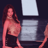 a woman in a gold top and black shorts is dancing on stage