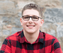 a man wearing glasses and a red and black plaid shirt smiles for the camera