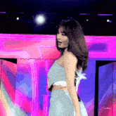 a woman in a crop top and skirt is dancing on a stage with a pink background