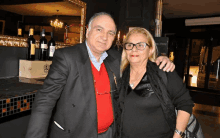 a man and woman are posing for a picture in front of bottles of wine and a sign that says " l' amore "