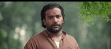 a man with a beard and a red mark on his forehead is standing in the woods .