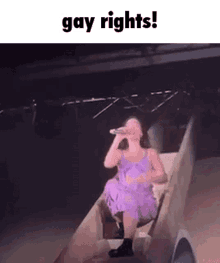 a woman in a purple dress is singing into a microphone while riding down a slide .