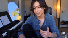 a young man sitting in front of a piano holding a cell phone and smiling